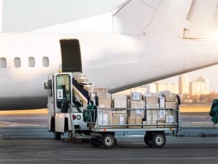 Close-up detail view of cargo cart trolley full with commercial parcels against turboprop cargo plane. Air mail shipping and logistics. Import export operations. Commercial charter flight service.