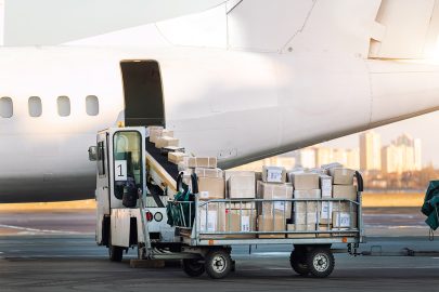 Close-up detail view of cargo cart trolley full with commercial parcels against turboprop cargo plane. Air mail shipping and logistics. Import export operations. Commercial charter flight service.